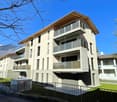 modern white building, several floors, balconies, metal railings, outdoor air conditioning units, fenced yard