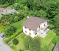 Two story house, white walls, brown roof, 4 windows, balcony, driveway, stone steps, car parked, grass garden