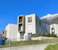 Modern apartment building with white walls, brown accents, multiple windows, and a playground in front.