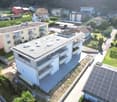 Aerial view of a residential building with multiple balconies, solar panels on the roof, and a car parking area.