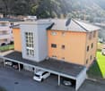 3 story house, orange and white, 3 cars in garage, green lawn, mountain in background