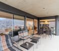 Outdoor terrace with white tiles, large sliding glass doors, reclining chairs, tables, scenic mountain view