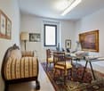 Wooden desk with two chairs, glass table, rug, a lamp, wooden couch, pictures, and paintings on the wall