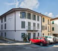 2 story white building, multiple windows, balcony on second floor, cars parked in front