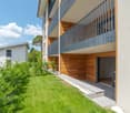 modern residential building, multi-story, metal and wooden balconies, entrance with large windows, grass garden