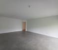 Large, open room with gray tile flooring, white walls, and a doorway leading to another room.