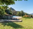 Large open grassy area with a swimming pool, concrete steps leading to the building, surrounded by greenery and distant hills