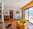 Spacious living room with large windows offering a scenic view, yellow and blue color scheme, wooden furniture, bookshelves, and a balcony or terrace access