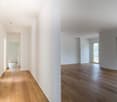 Spacious apartment with hardwood floors, large windows, and an open floor plan. The apartment features a hallway leading to various rooms and a main living area with a view of the surrounding landscape.