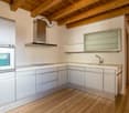 Spacious kitchen with wooden beamed ceiling, white cabinets, stainless steel appliances including a range hood and dishwasher, and hardwood flooring.