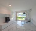 Spacious living room with large windows overlooking a scenic outdoor view, modern white furniture including a TV stand and dining table, and sleek tile flooring.