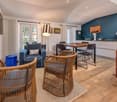 blue couch, wooden table, wooden chairs, television, kitchen with modern appliances