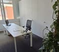 an empty office room with a desk, two office chairs, computer monitors, a cabinet, a window with view to a building