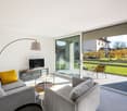 modern living room with gray couches, glass table, TV, floor lamp, sliding glass doors to terrace