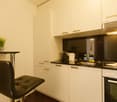 Compact kitchen with white cabinets, black countertops, and a dishwasher. There is a small table with a chair in the corner.