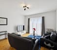 two black leather couches, tv, center table, wooden floor, wall decor, two white shelves, radiator