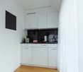 Open concept kitchen with white cabinetry, granite countertops, built-in appliances, wooden floor, black tile backsplash