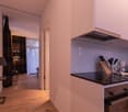 Minimalist kitchen area with wooden floor, black countertops, white cabinetry, a kitchen island, and a black oven with a range hood.