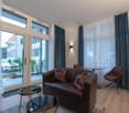 modern apartment, large windows, sliding glass doors, hardwood floor, brown sofa, brown chairs, small table, brown cushions