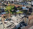 Aerial view of a construction site of a residential building, surrounded by existing houses and a crane in the middle