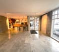 wide entrance hall with marble tiles, brick wall, open kitchen with wooden bar and island, sliding door to outside, 2 bar stools, double doors, open kitchen with oven, fridge, cabinets, countertop, large windows, outdoor table and grill, parked car