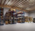 Large warehouse with high ceilings, steel shelves, forklifts, and people carrying pallets. Bright with lights on the ceiling, clear blue floor.