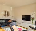 black leather couch with pillows, flat screen TV, carpet, black modern chair, white cabinet with TV, decorative pillow, modern lamps, wooden floor