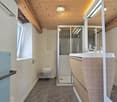 modern bathroom with wooden ceiling, white walls, gray floor, glass shower, white toilet, white sink, wooden cabinet, mirror