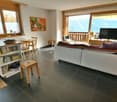 Living room with sofa, table, chairs, kitchen island, TV, windows, balcony, wooden flooring, wooden furniture, open shelves, carpet