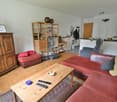 Spacious living room with hardwood floors, white walls, wooden shelving unit, antique cabinet, red leather sofa, coffee table, and various decor items