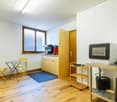 Wooden floor, white walls, round table with two chairs, blue rug, kitchen appliances, refrigerator, microwave