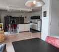 modern kitchen with dining area, wooden floor, white and black color scheme, kitchen island, modern appliances, potted plants, chandelier, red cushions on bar stools