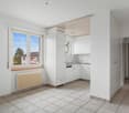 Empty kitchen with white tiles, white kitchen units, a sink, and a window.
