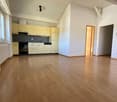 Empty room with wooden floor, white walls, kitchen with cabinets, sink, and dishwasher, windows, and a door.