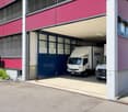 A warehouse building with two trucks parked inside, two automated doors, a red and white design, and metal panels.