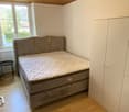 bedroom with bed, nightstand, wardrobe, wooden floor, white walls, window