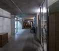 Long, dimly lit concrete hallway with wire mesh fencing on one side and various storage items along the walls.