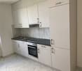 Modern, minimalist kitchen with white cabinets, marble-patterned backsplash, built-in oven and dishwasher, and stainless steel sink