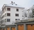 3-story white apartment building with brown shutters, garage doors, and a snowy roof