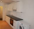 White kitchen cabinets, black countertop, built-in oven, washing machine, dishwasher