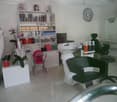 The image shows a hair salon with various hair care products and equipment. There is a shelving unit with numerous hair products, a sink and chair for hair washing, and a styling chair. The room also has decorative elements like a mirror and plants.