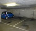 Underground parking space with a blue car, white markings, concrete walls, and a ceiling light