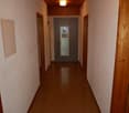 Empty hallway with wooden floor, white walls, wooden ceiling, doors on both sides, and a light on the ceiling.