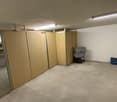 Empty room with white walls, ceiling lights, wooden storage units, and a shelf with items