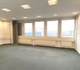 Empty room with windows, wooden door, radiators, and a city view.
