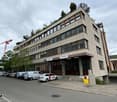 5 story building, many windows, multiple cars parked, signboard on front
