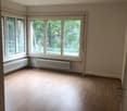 Spacious living room with large windows overlooking a wooded area, hardwood floors, and neutral wall colors