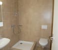 Modern and compact bathroom with a shower, toilet, and sink. Tiled walls and floors.