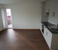 Empty kitchen, wooden floors, white walls, black countertops, stainless steel sink, built-in appliances, large windows with a balcony view.