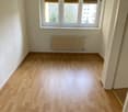 Empty room with wooden floor, white walls, windows with blinds, white radiator